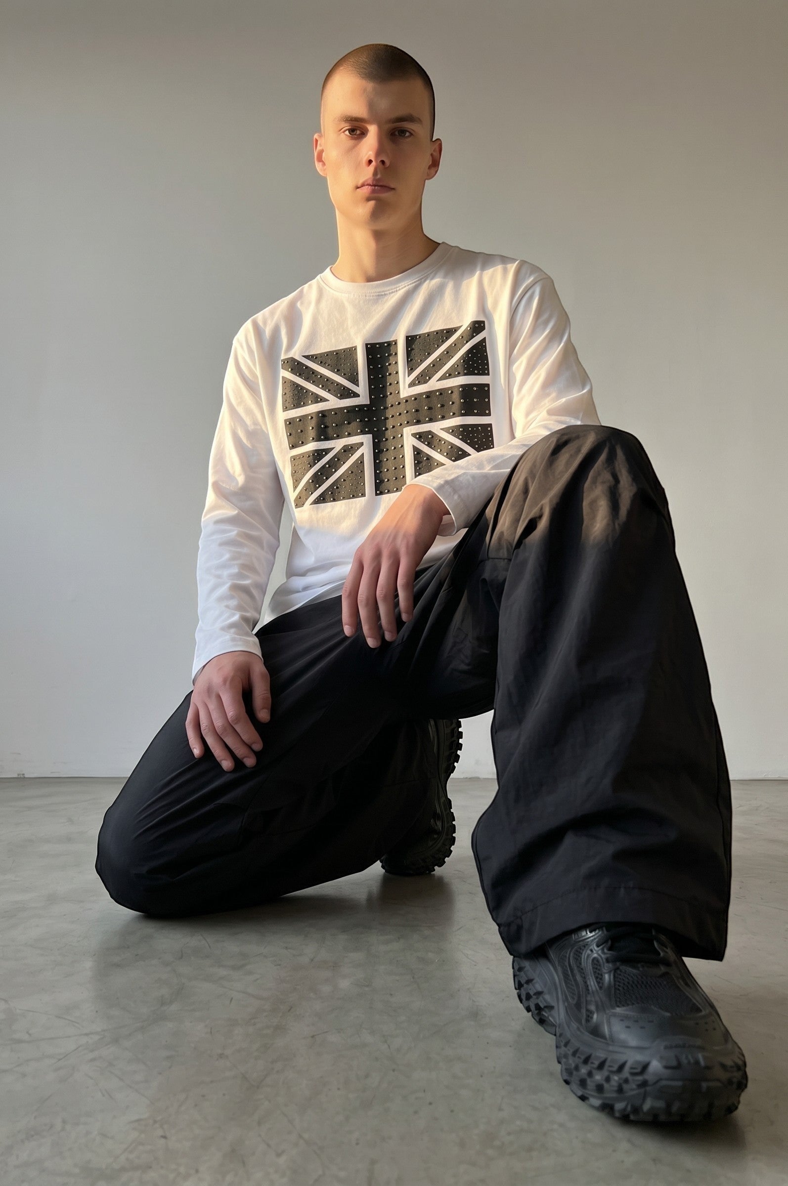 Camiseta blanca de manga larga Estudio Mora con estampado de Union Jack en negro y tachuelas. Pantalones negros anchos.