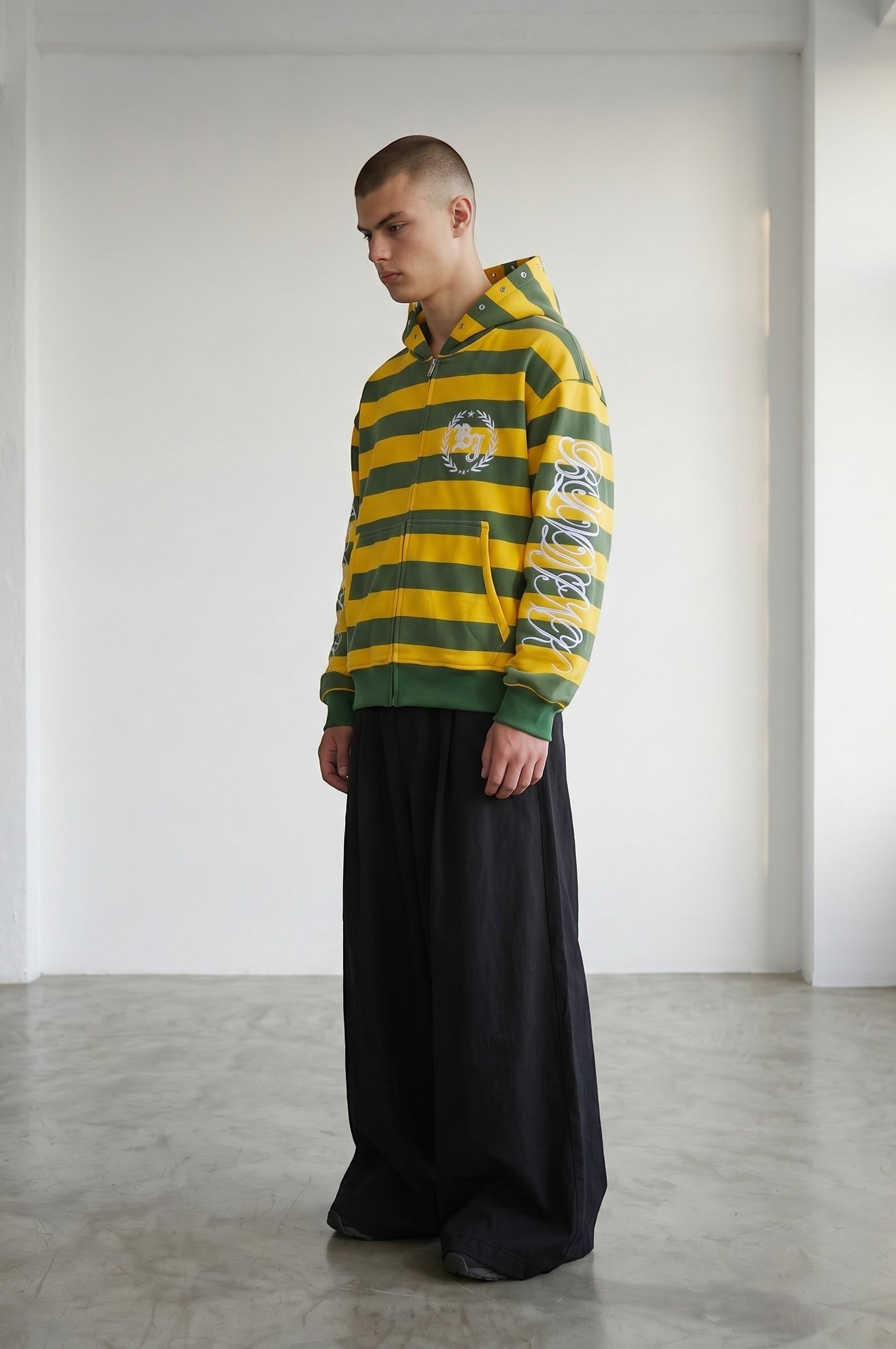 Estudio Mora Funky Zip-Up sudadera con cremallera a rayas verdes y amarillas, con logo en el pecho y estampado en la manga.