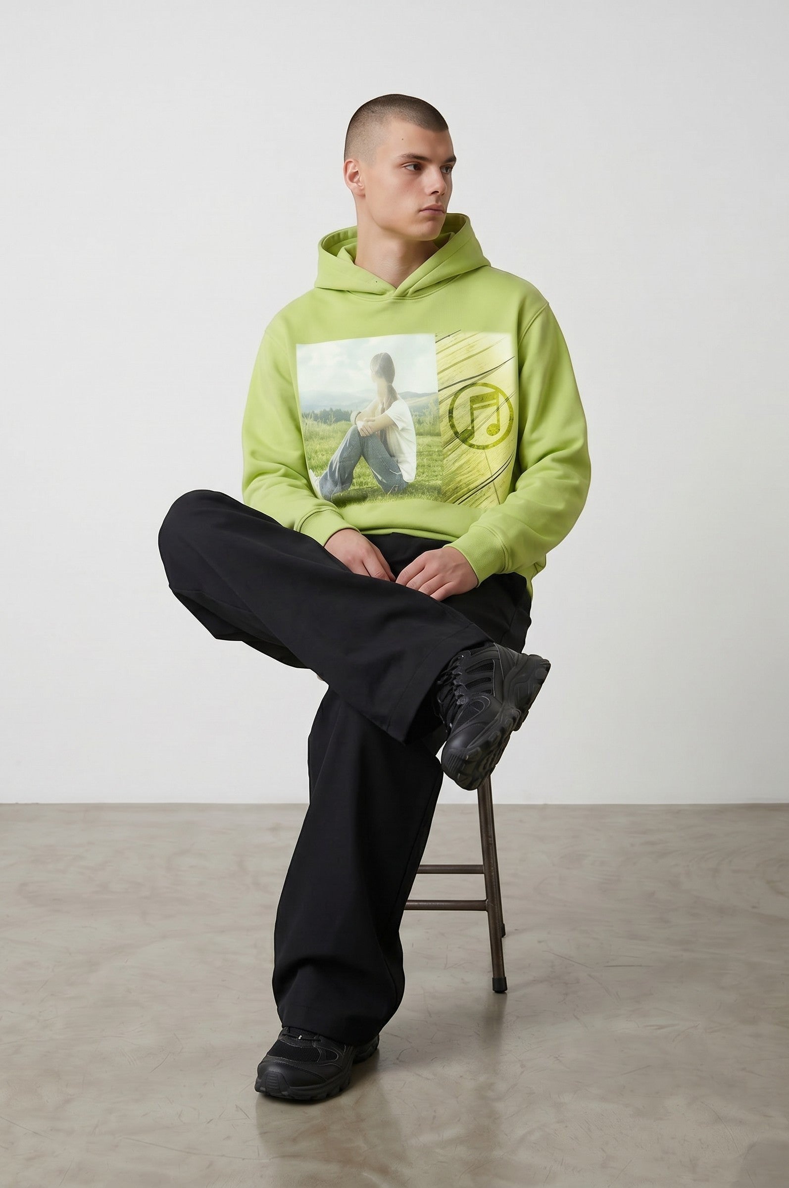 Sudadera con capucha verde lima de Estudio Mora con estampado de imagen y nota musical. Modelo masculino sentado.