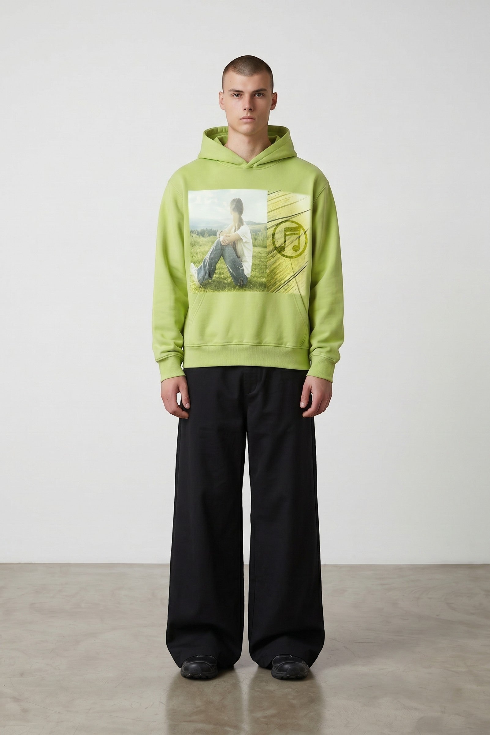 Sudadera con capucha verde lima de Estudio Mora con estampado gráfico de nota musical y persona sentada en un prado.