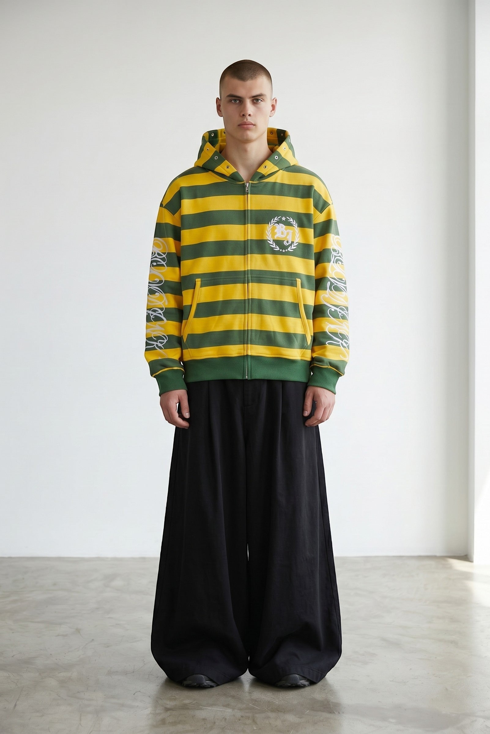 Sudadera con cremallera de Estudio Mora a rayas verdes y amarillas con logo en el pecho y estampado en las mangas.