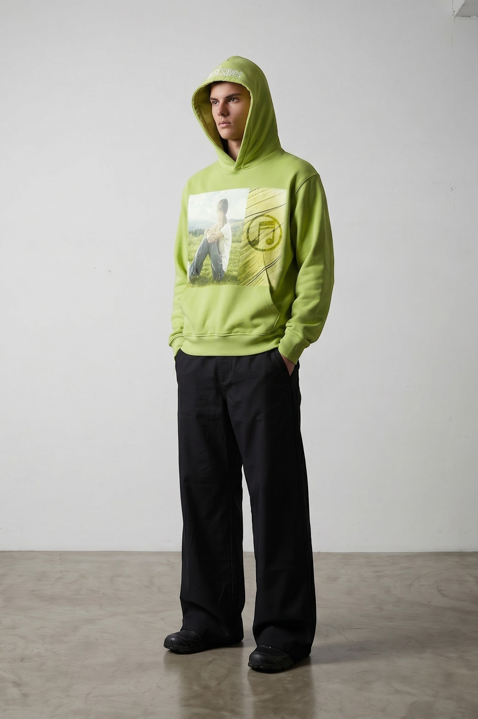 Sudadera con capucha verde lima de Estudio Mora con estampado gráfico de un niño sentado en un campo y una nota musical.